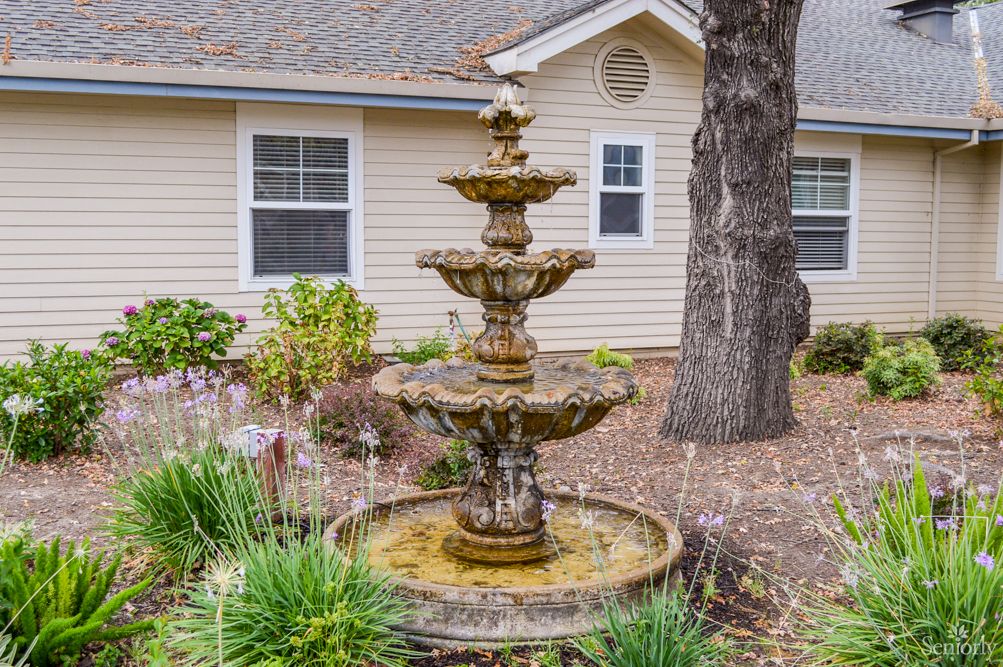 A three-tiered fountain stands in a landscaped garden in front of a house.