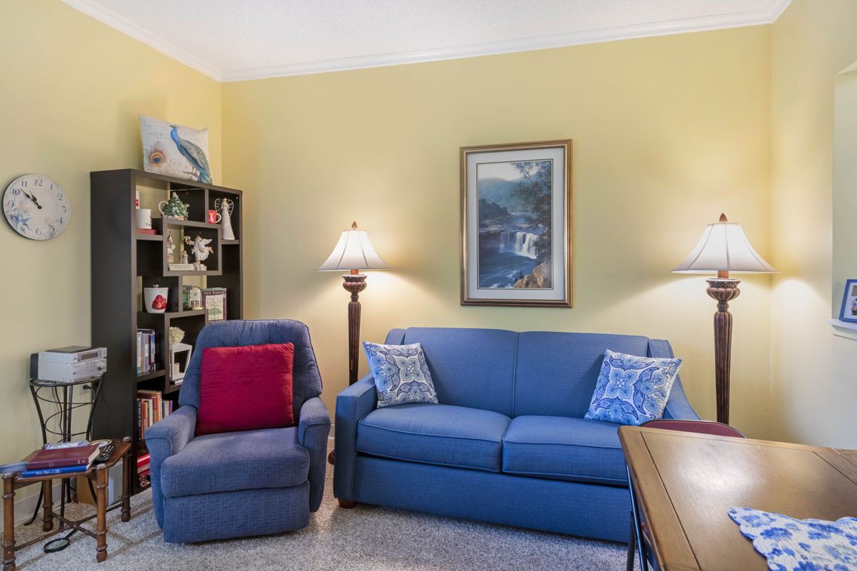 A cozy living room with a blue sofa, comfy chair, and a bookshelf.
