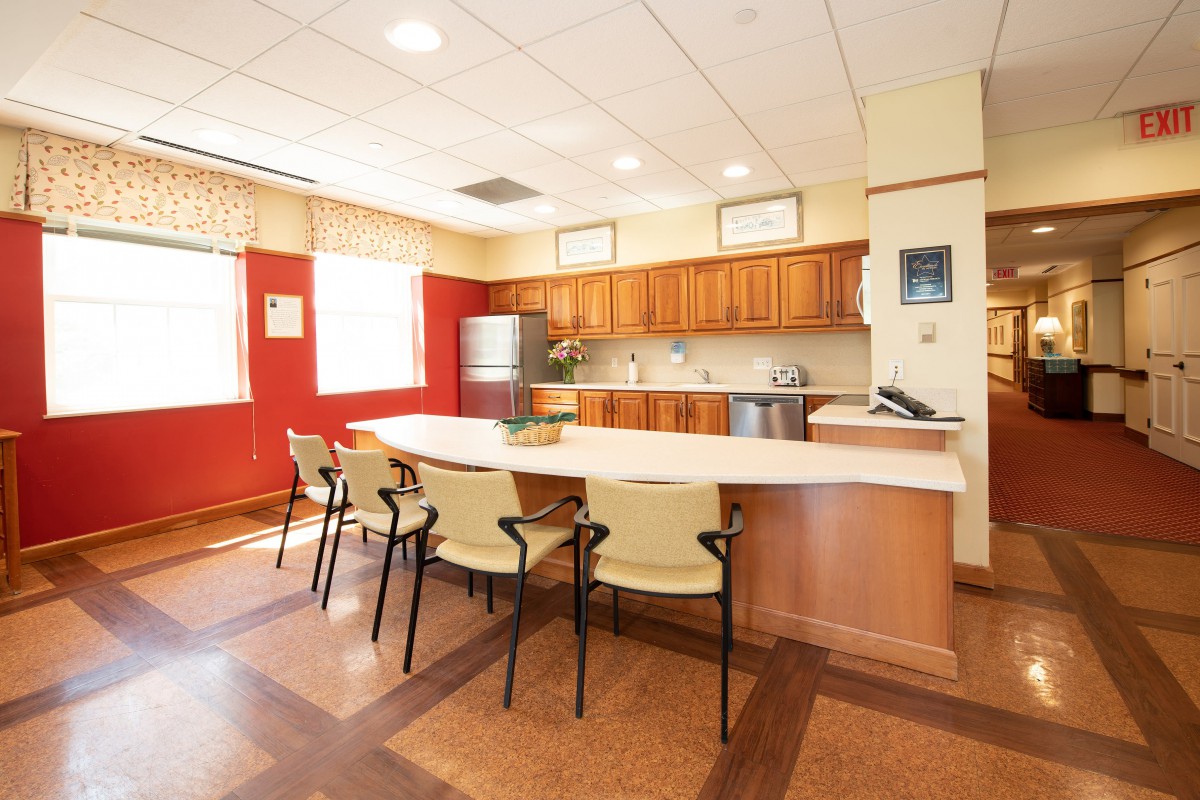 A modern kitchen and meeting area with wooden cabinetry and a central counter surrounded by chairs.