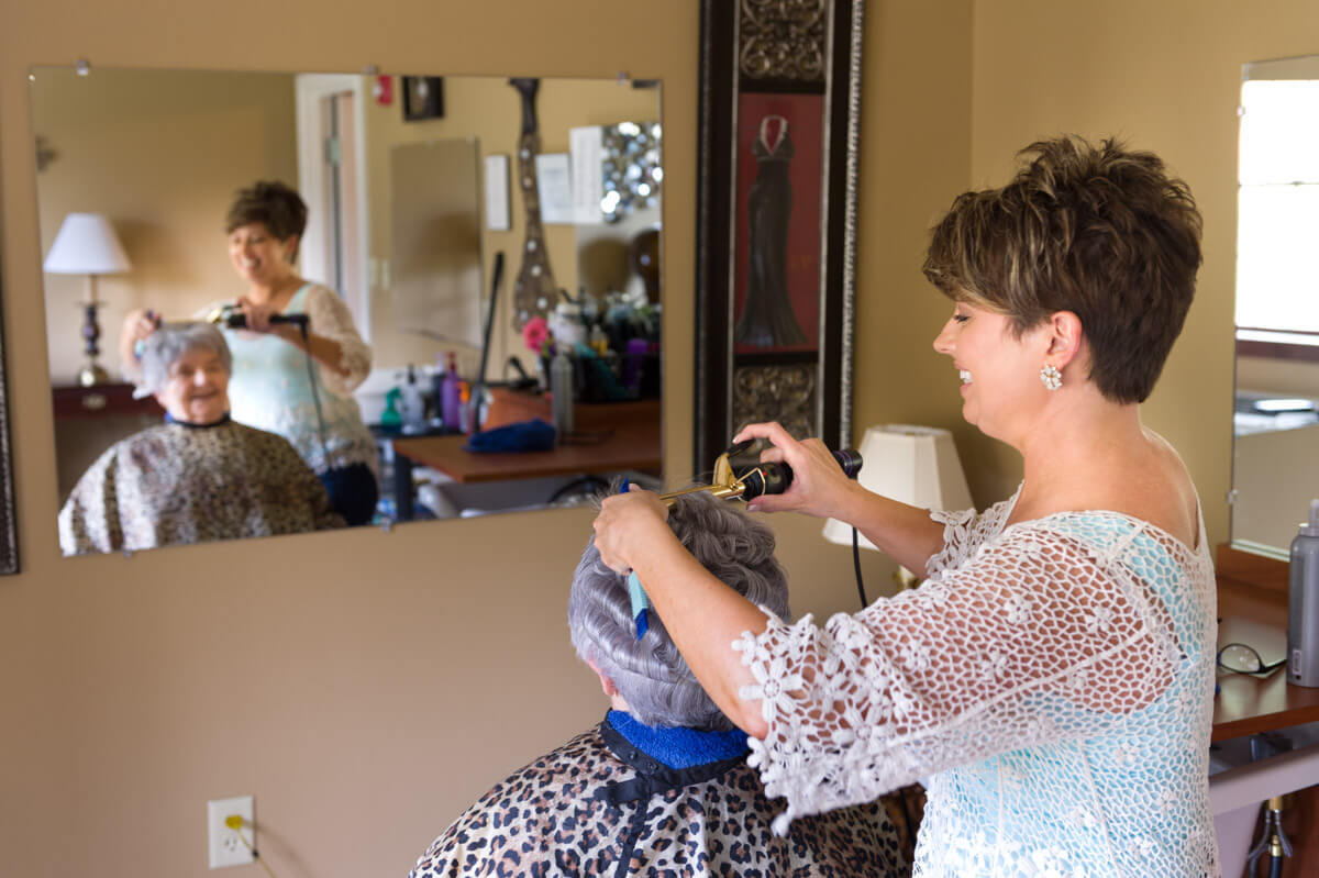A hairdresser styling a client's hair in a salon, with reflections visible in the mirror.