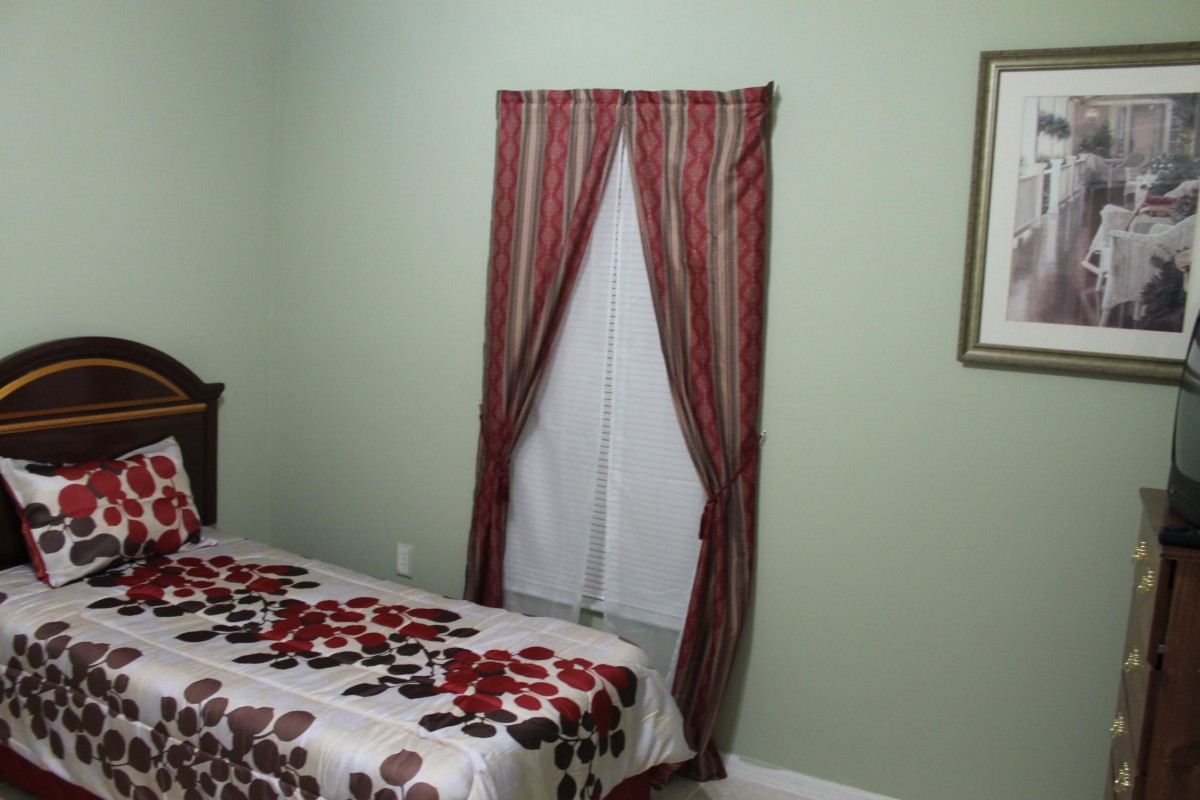 A bedroom with a bed featuring a floral bedspread and a window adorned with red striped curtains.