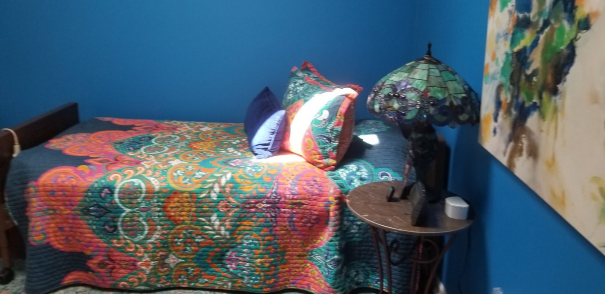 A cozy bedroom with a colorful quilt, decorative pillows, and a lamp on a side table.