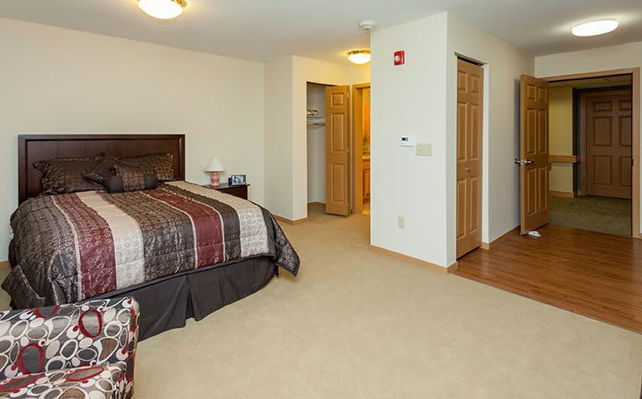 A cozy bedroom featuring a large bed with a patterned comforter, carpeted flooring, and an open closet in the background.
