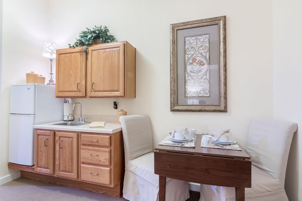 A cozy kitchen corner with wooden cabinets, a small dining table set for two, and artwork adorning the wall.