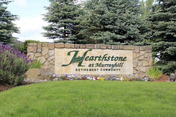 A sign for Hearthstone at Murrayhill Retirement Community surrounded by a stone wall and greenery.