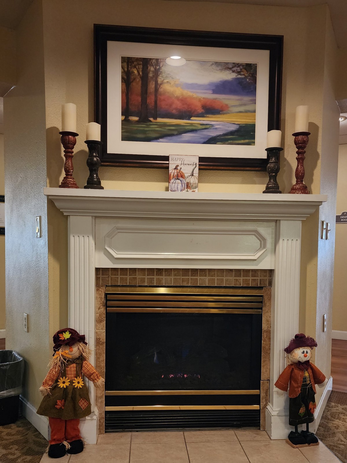 A cozy fireplace decorated with autumn-themed items, including scarecrow figures and candles on the mantel.