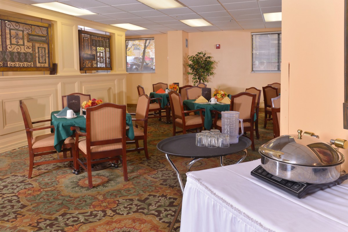 A cozy dining area with neatly arranged tables and chairs, featuring a patterned carpet and warm lighting.