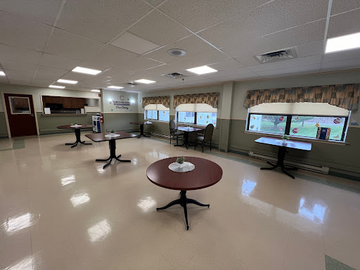 A spacious indoor area featuring several round tables, large windows, and a clean floor.