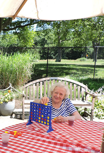 An elderly woman enjoys a game of Connect Four on a sunny day, surrounded by nature.