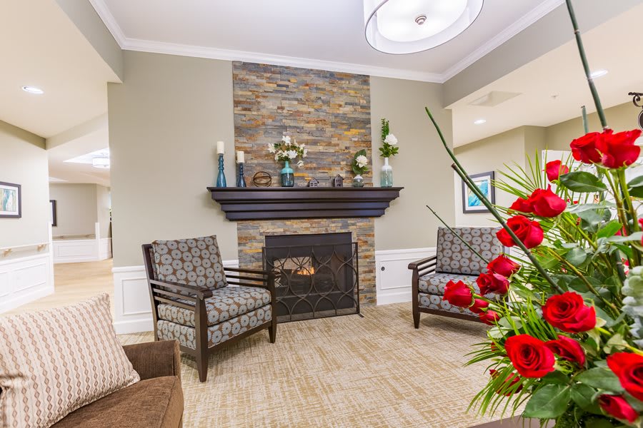 A cozy living room with a stone fireplace, accented by two patterned chairs and vibrant floral decor.