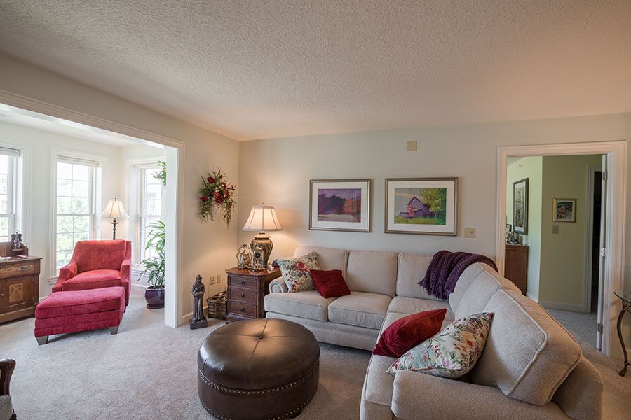 A cozy living room with a beige sectional sofa, colorful pillows, and wall art, accented by a lamp and decorative items.