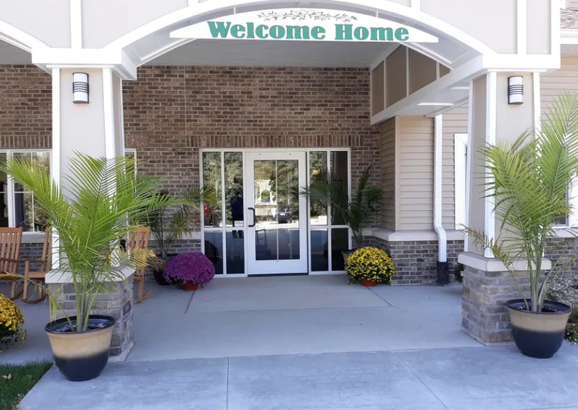 A welcoming building entrance with potted plants and a 'Welcome Home' sign above the door.