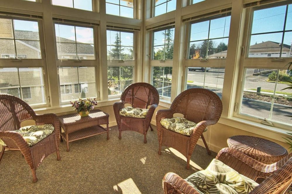 A bright and cozy sunroom featuring wicker furniture and large windows.