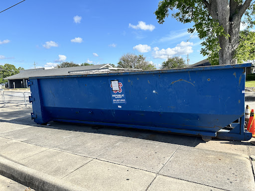 A blue dumpster on the side of the street under a clear sky.
