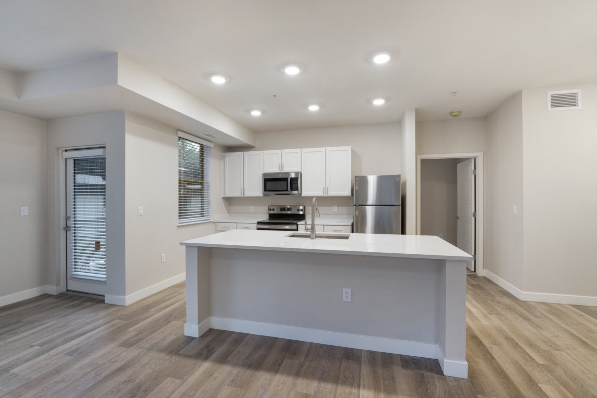 A modern kitchen with an open concept design featuring a central island, stainless steel appliances, and recessed lighting.