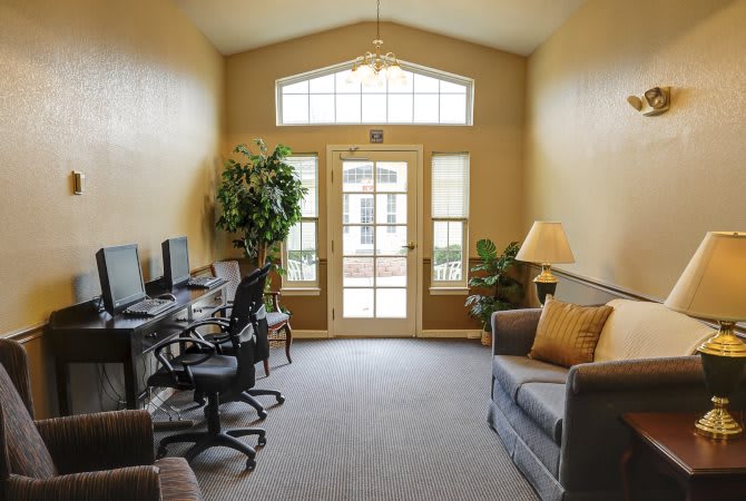 A cozy dual-purpose room featuring a blend of living and office space with comfortable seating, computers, and natural light.