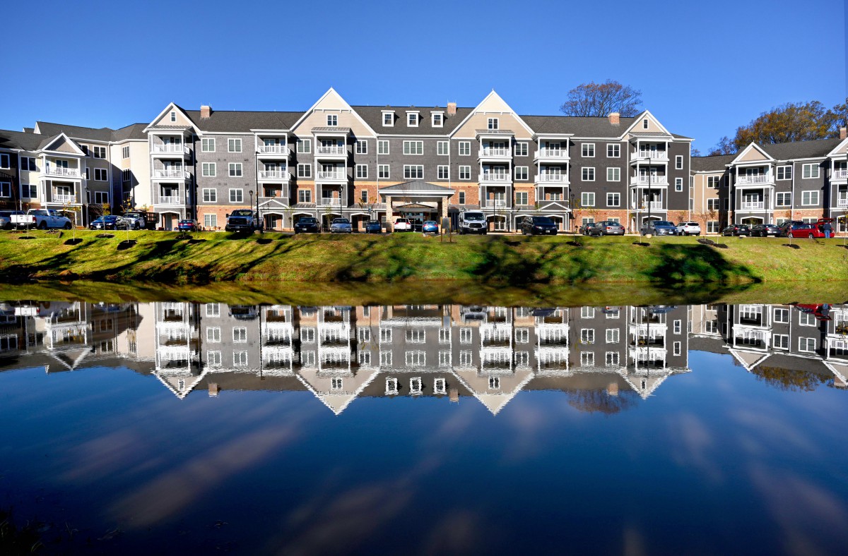 A residential building with a symmetrical reflection on a calm lake under a clear blue sky.