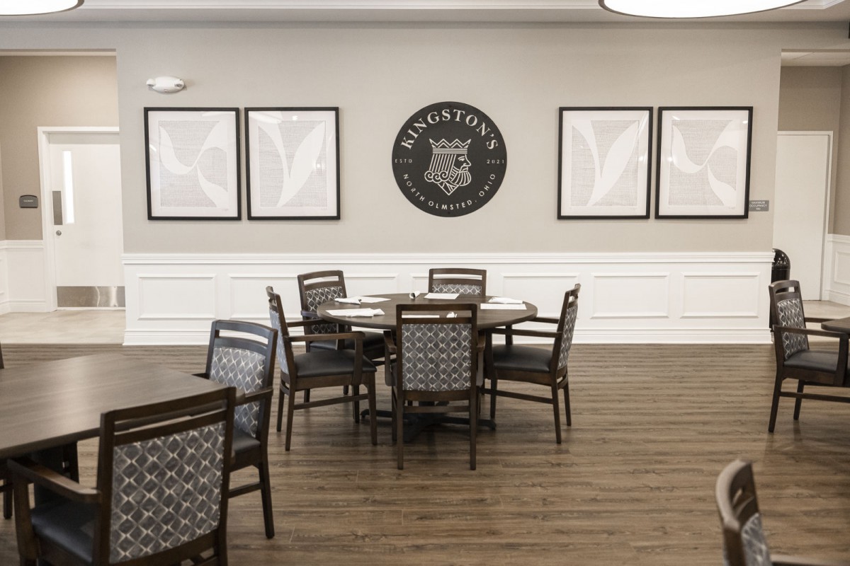 A minimalist dining area with wooden tables and chairs, featuring decorative wall art and a polished wooden floor.