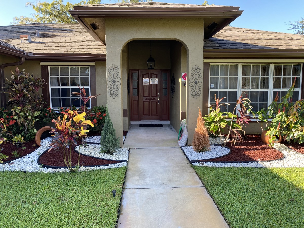 A well-maintained front yard with a pathway leading to the entrance of a house, surrounded by landscaped gardens.