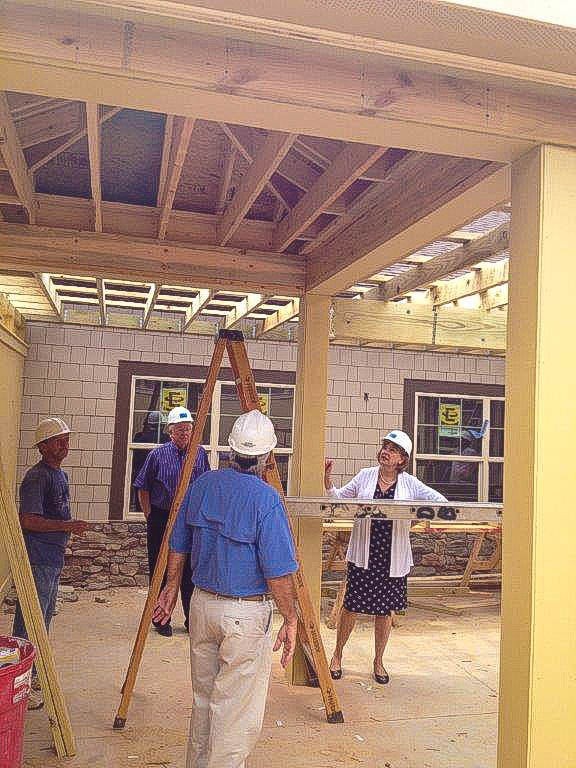 A group of construction workers wearing hard hats are inspecting a building under construction, with wooden framework and a ladder visible.