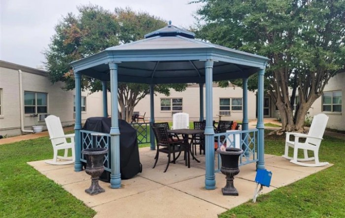 A blue gazebo with outdoor seating and a covered grill, set in a garden area.