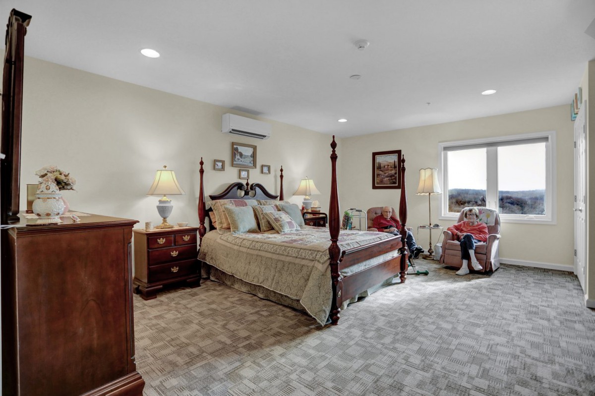 A spacious bedroom featuring a four-poster bed, elegant furniture, and soft carpeted flooring.