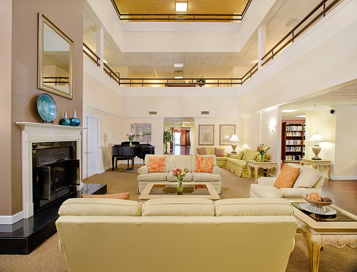 A spacious and elegantly decorated living room with multiple seating areas, a grand piano, and a fireplace.