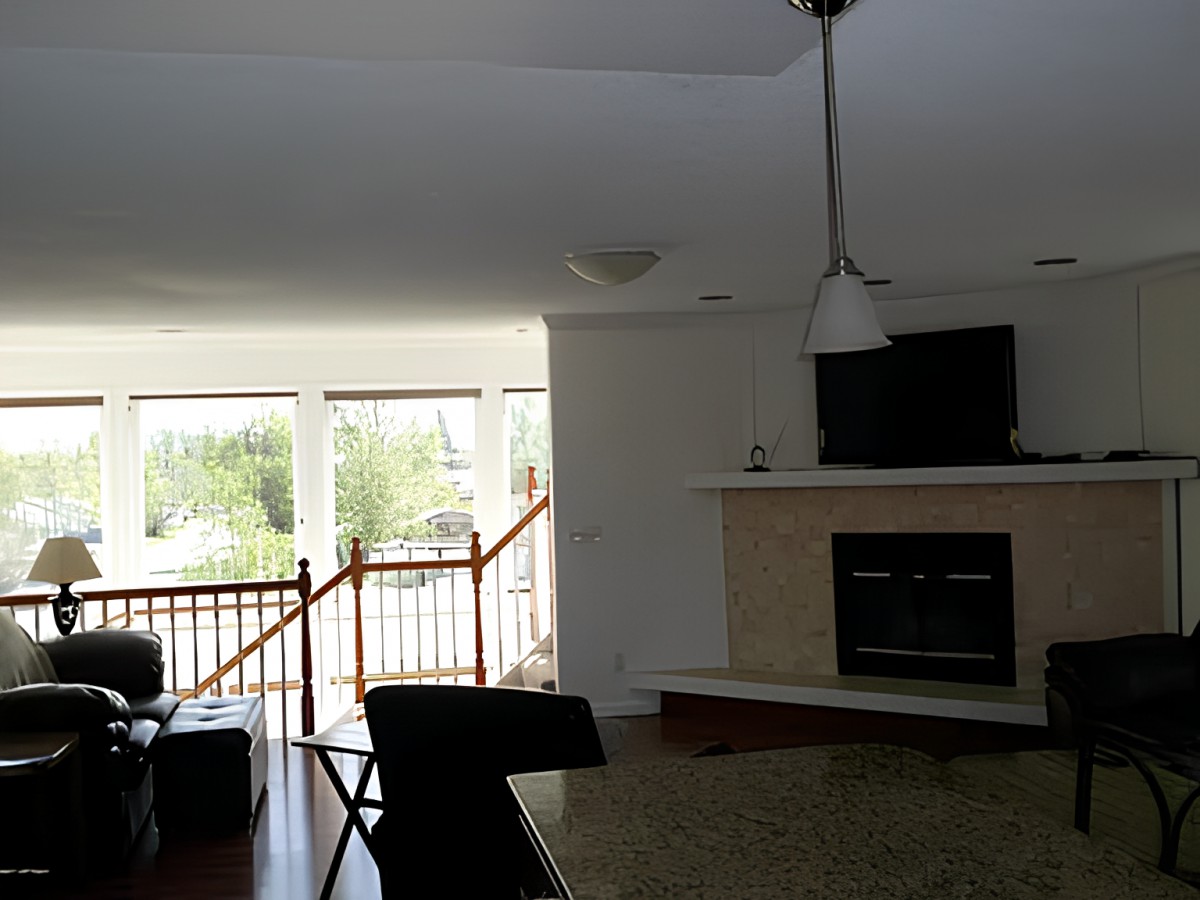 A cozy living room with a fireplace and television, featuring large windows and stairs leading upwards.