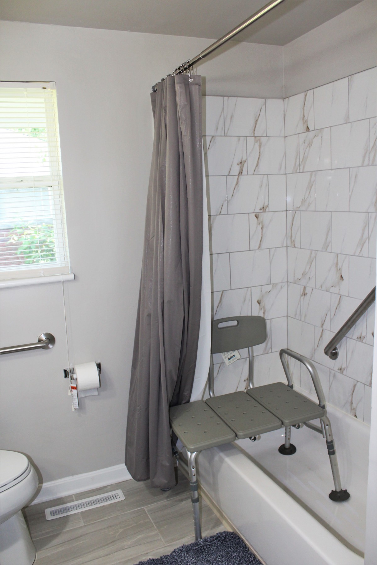 A bathroom with a tiled shower area featuring a shower chair and grab bar for accessibility.