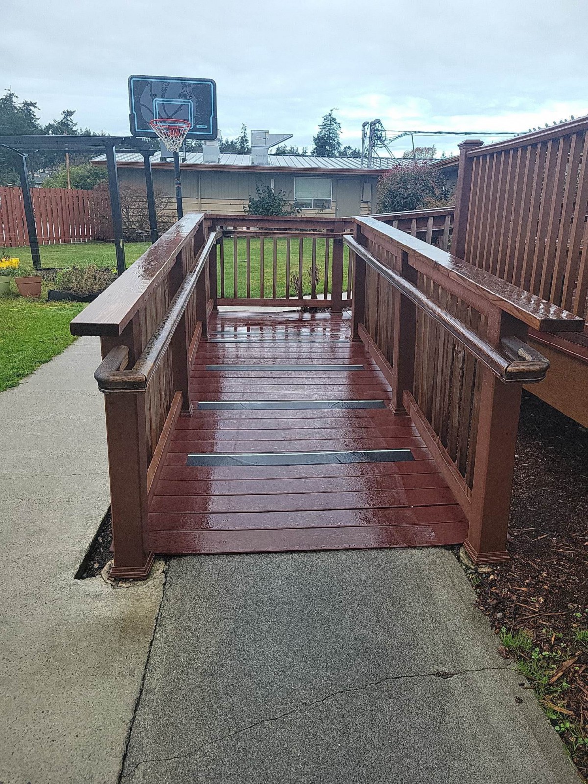 A wooden accessibility ramp leading to a deck, surrounded by greenery.