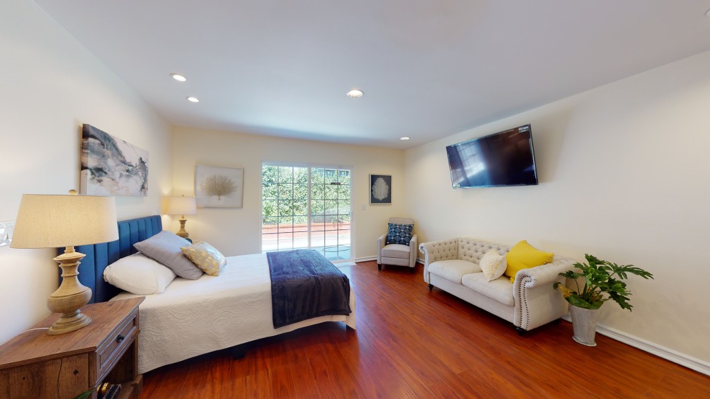 A modern bedroom with wood flooring, featuring a comfortable bed, sofa, and wall-mounted TV.