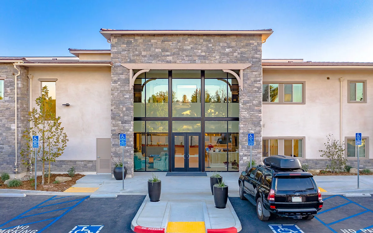 A modern building entrance with a glass facade and stone exterior, accompanied by a parking lot.