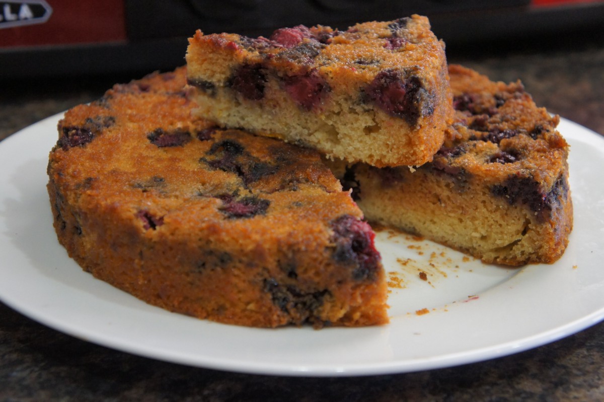 A homemade berry cake with a slice cut out and placed on top.