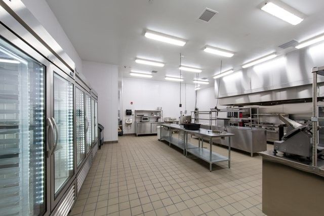 A spacious commercial kitchen with stainless steel equipment and large refrigerators, featuring clean tile flooring.