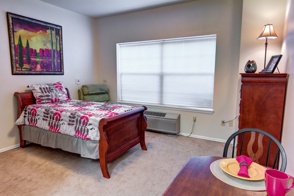 A cozy bedroom with a single bed, decorated with colorful bedding and a large window letting in natural light.
