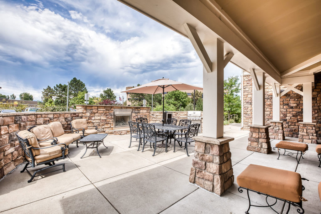 A cozy outdoor patio with comfortable seating and an umbrella under a partly cloudy sky.