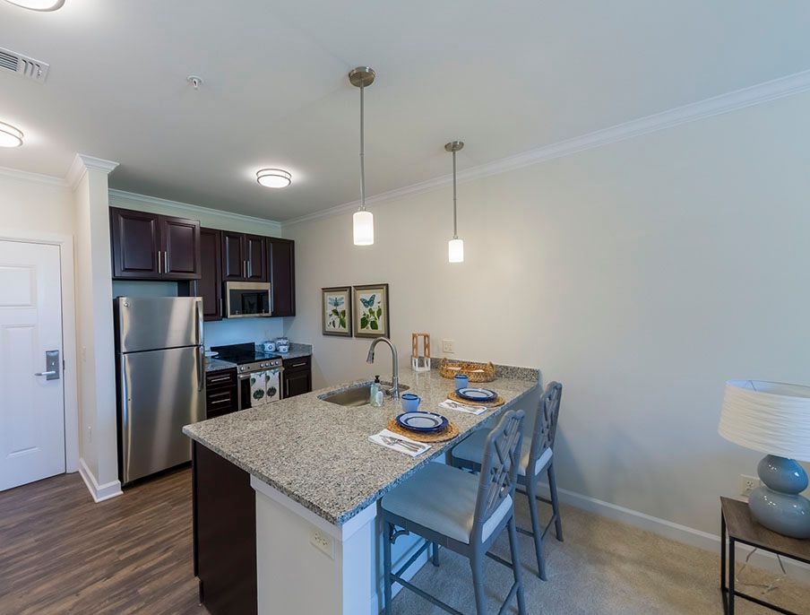 A modern kitchen with a granite countertop and stainless steel appliances, featuring pendant lighting and bar stools.