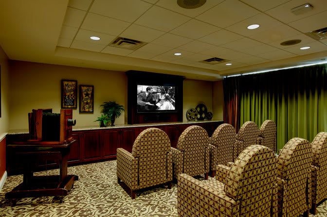 A cozy home theater room with patterned seats facing a screen displaying a black and white film.
