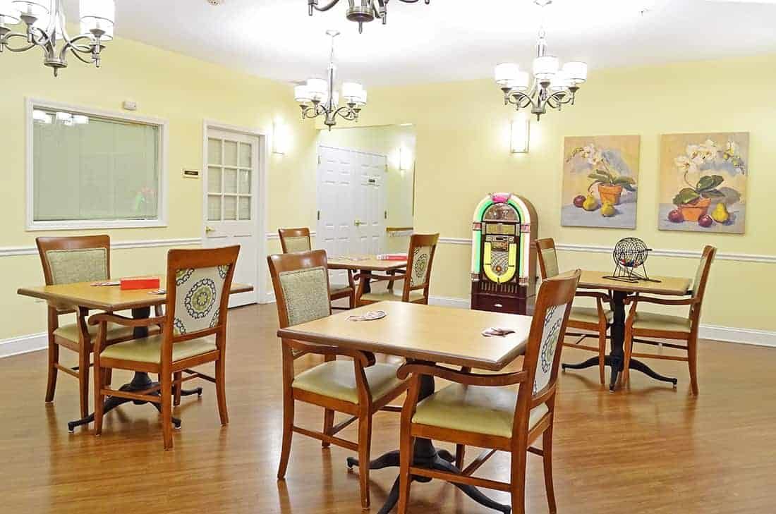 A brightly lit dining area with wooden tables and chairs, featuring a jukebox in the corner.