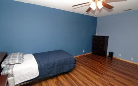 A minimalist bedroom with blue walls, featuring a single bed and wooden flooring.
