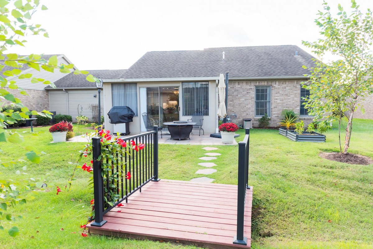A cozy backyard with a small bridge leading to a patio area of a suburban house.