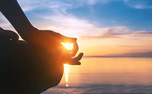 A serene sunset scene with a hand forming a meditation gesture.