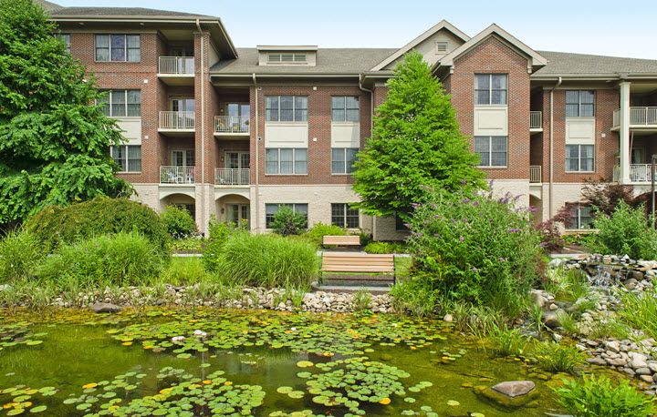 A view of an apartment building with a scenic pond and lush greenery in the foreground.