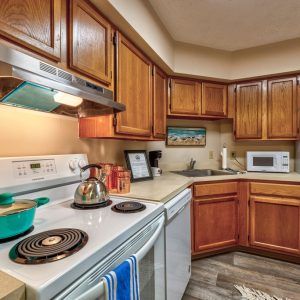 A cozy kitchen with wooden cabinets, featuring a stove, microwave, and teapot on the counter.