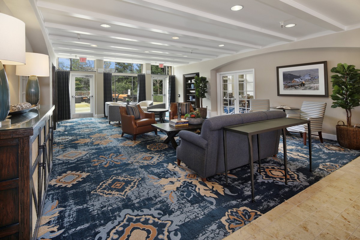 A spacious and well-lit lobby with comfortable seating and large windows, featuring a patterned carpet and stylish furniture.
