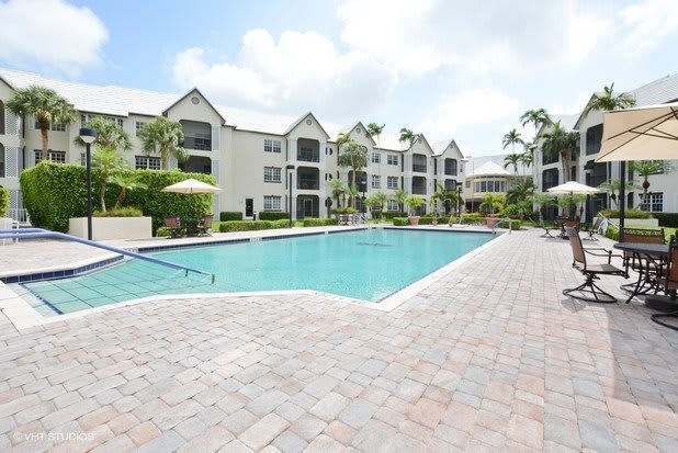 A view of an apartment complex with a large outdoor swimming pool surrounded by palm trees.