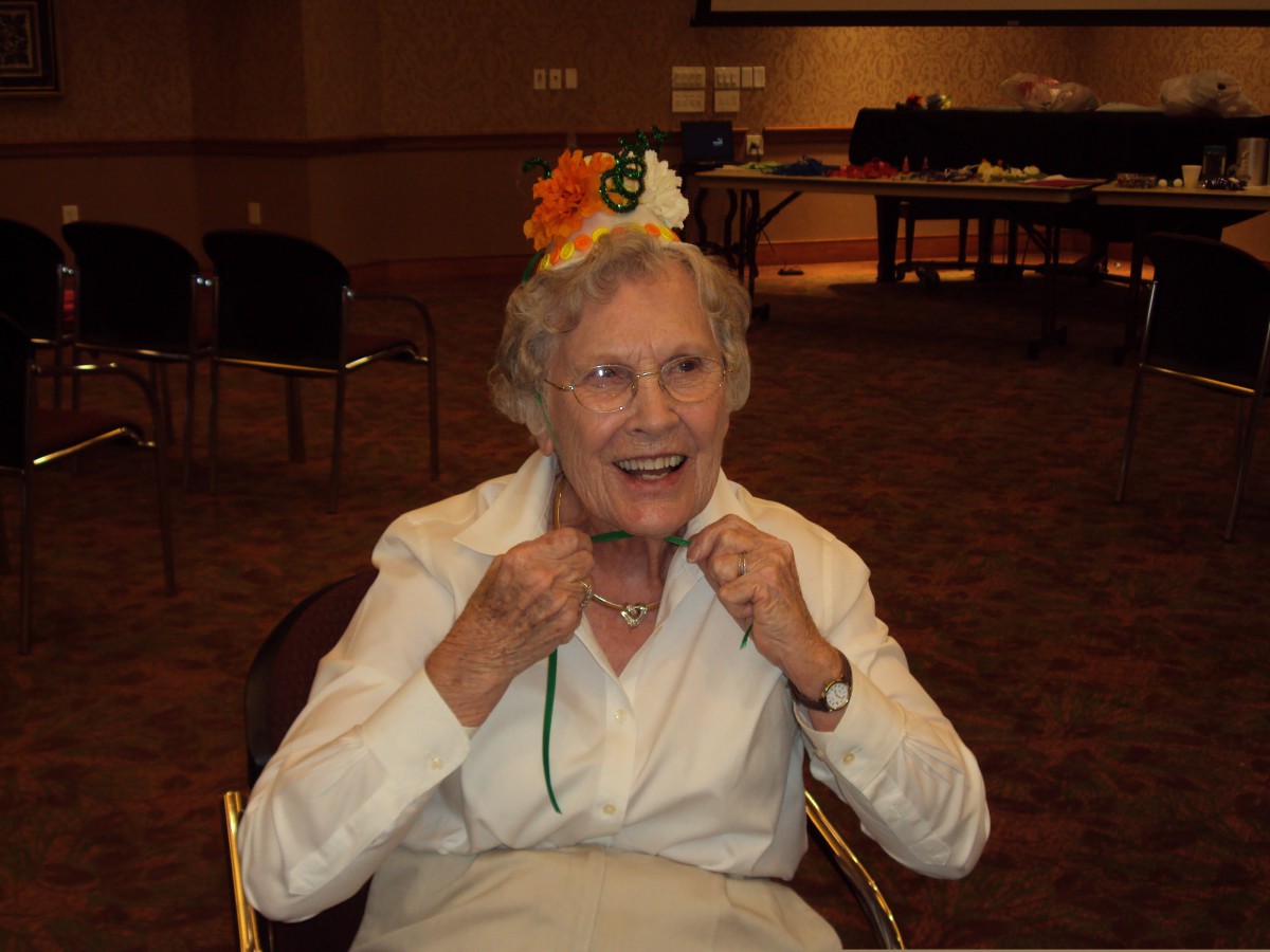 An elderly woman smiling and wearing a festive hat indoors.