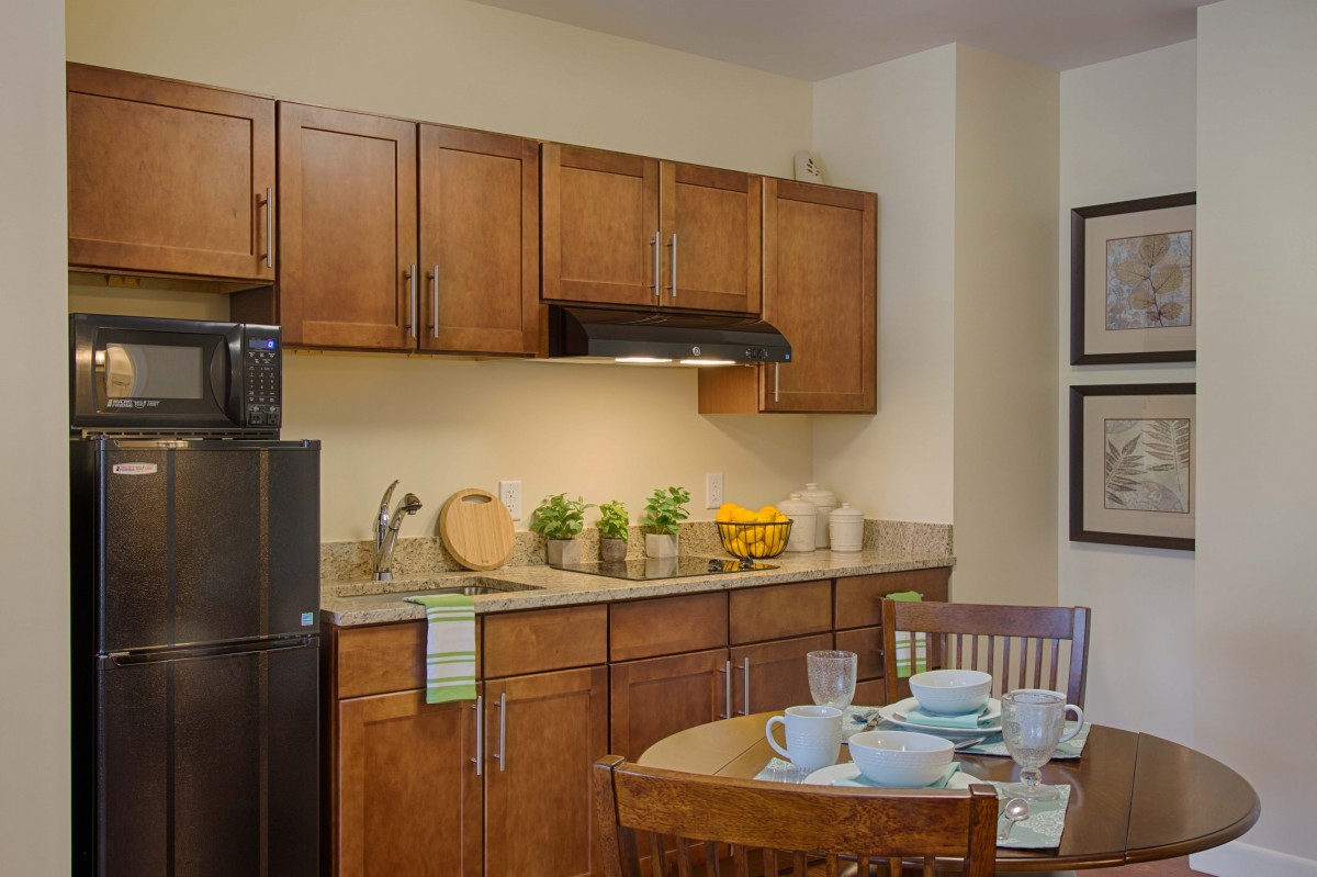 A modern kitchen interior featuring wooden cabinets, a dining table set with tableware, and various kitchen appliances.