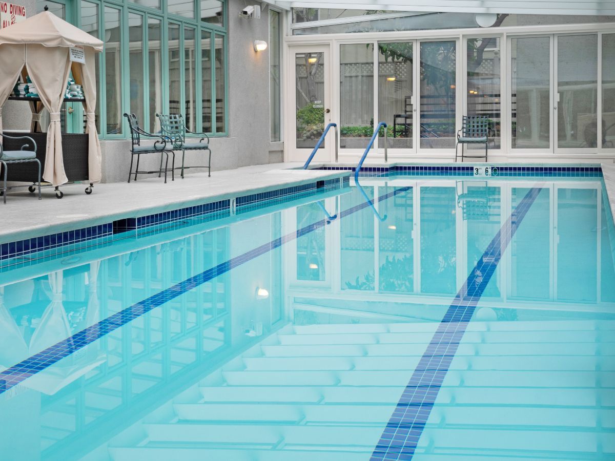 An indoor swimming pool with clear water and lane markings, surrounded by glass windows.