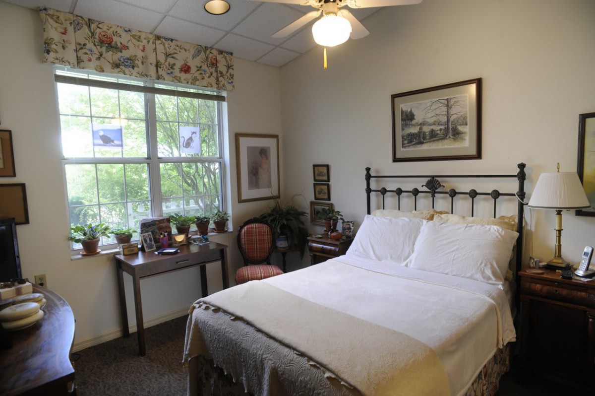A cozy bedroom with a neatly made bed, artwork on the walls, and a window letting in natural light.